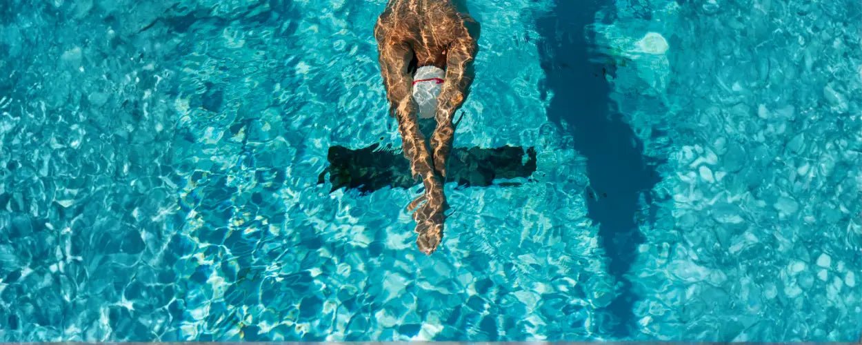 seorang perenang yang meluncur di permukaan air dengan posisi tubuh sejajar dan tangan lurus ke depan, menggambarkan awal gerakan dalam teknik renang gaya dada