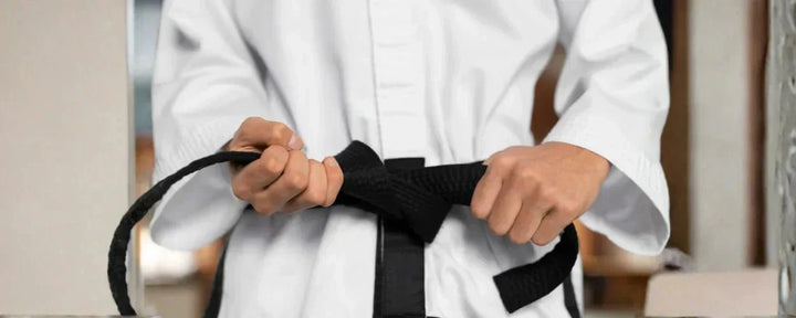 seseorang yang sedang mengikat sabuk hitam, melambangkan pencapaian tertinggi dalam tingkatan sabuk taekwondo yang menandakan disiplin dan keahlian tingkat lanjut.