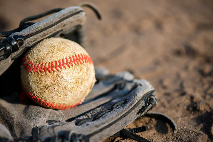 Sebuah bola dan glove softball terlihat berada di tanah, menjadi ilustrasi visual yang cocok untuk membahas tips dasar softball dalam konteks olahraga permainan bola.