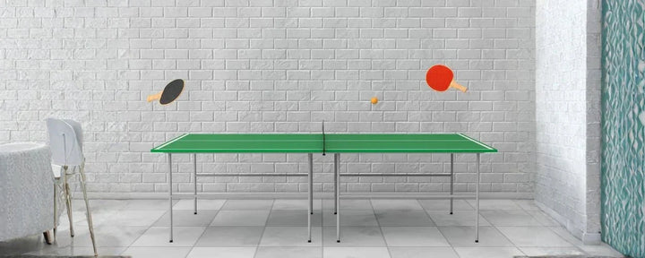 Meja tenis meja berwarna hijau lengkap dengan net, dua raket, dan bola, berada di ruangan dengan dinding bata putih