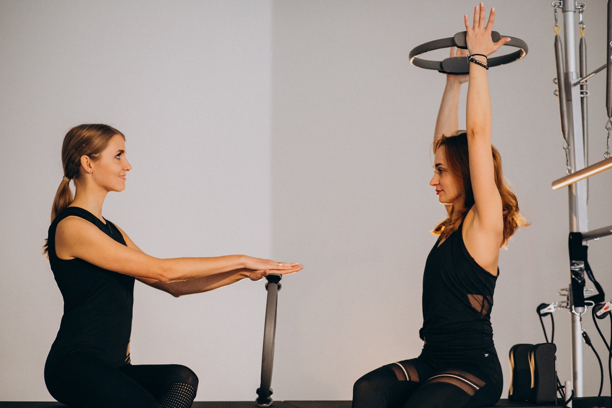 Dua wanita sedang menggunakan alat pilates ring saat sesi latihan bersama