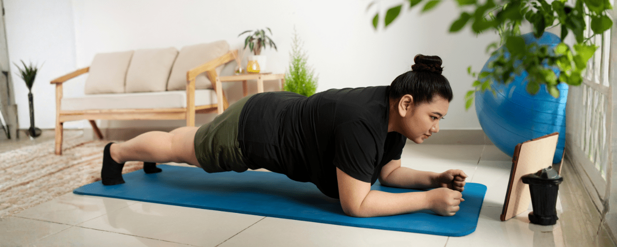 Seorang wanita sedang melakukan plank di atas matras biru sebagai bagian dari workout mengecilkan perut di rumah